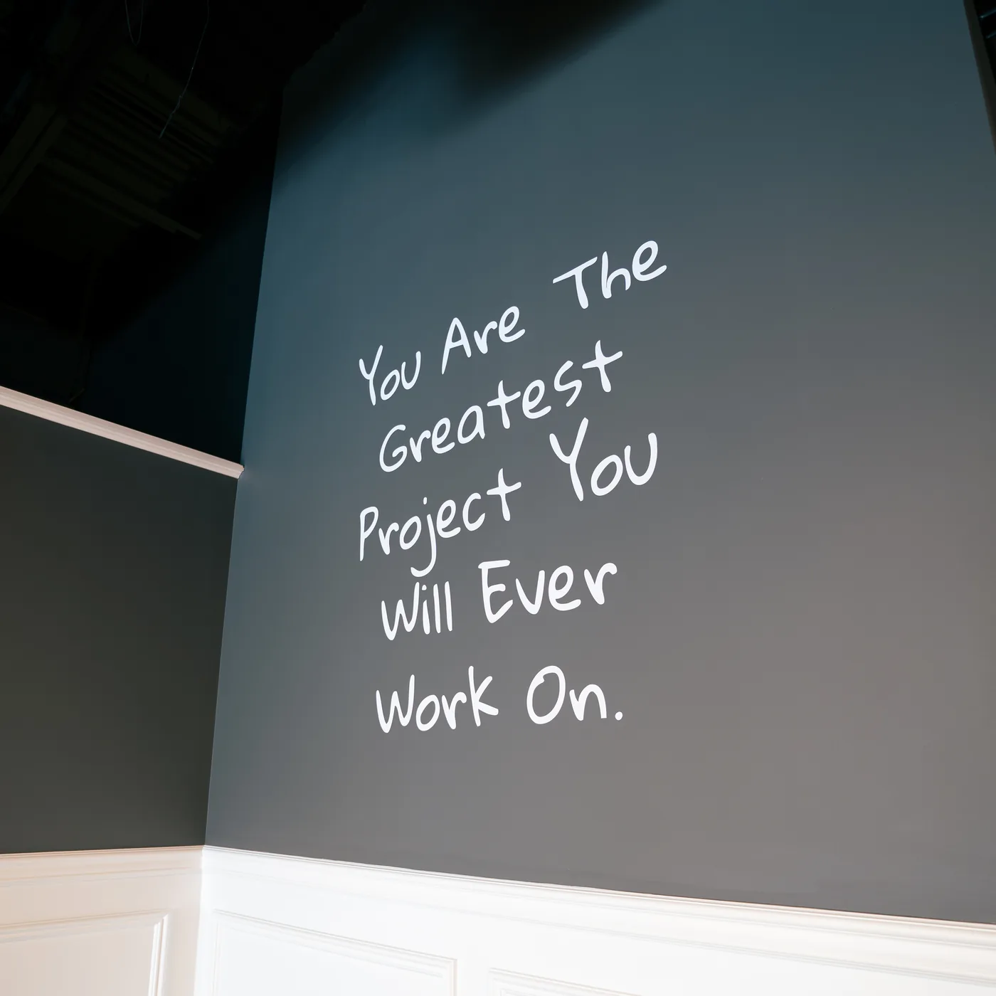 A dark grey wall inside Red Light Method Commack hand-lettered with the words You Are The Greatest Project You Will Ever Work On.