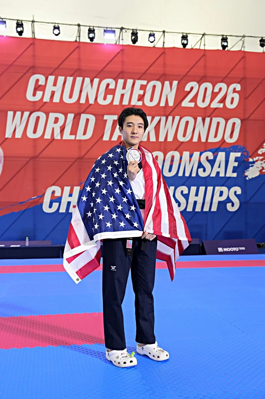 Preston Park wrapped in an American flag, holding up his silver medal in front of the Chuncheon 2026 World Taekwondo Poomsae Championships banner.