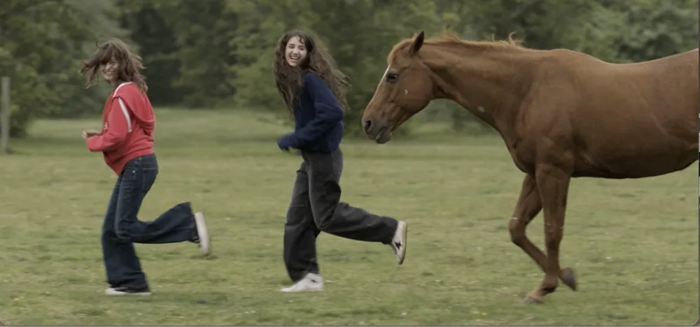 Two girls running alongside a horse through an open field on the North Fork
