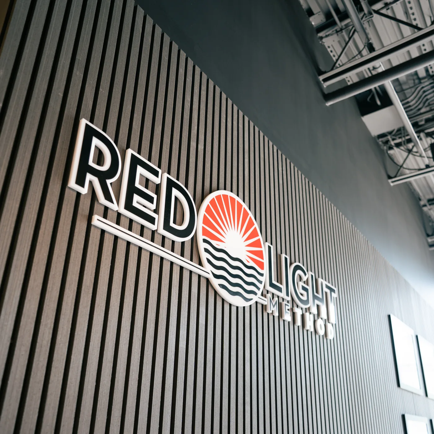 The Red Light Method logo mounted in dimensional lettering on a vertical black slat wall inside the Commack studio
