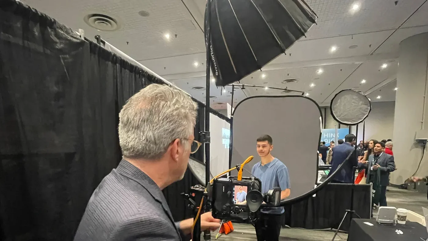Len Marks photographing a subject at an event, working behind a large softbox with the studio setup built on the floor