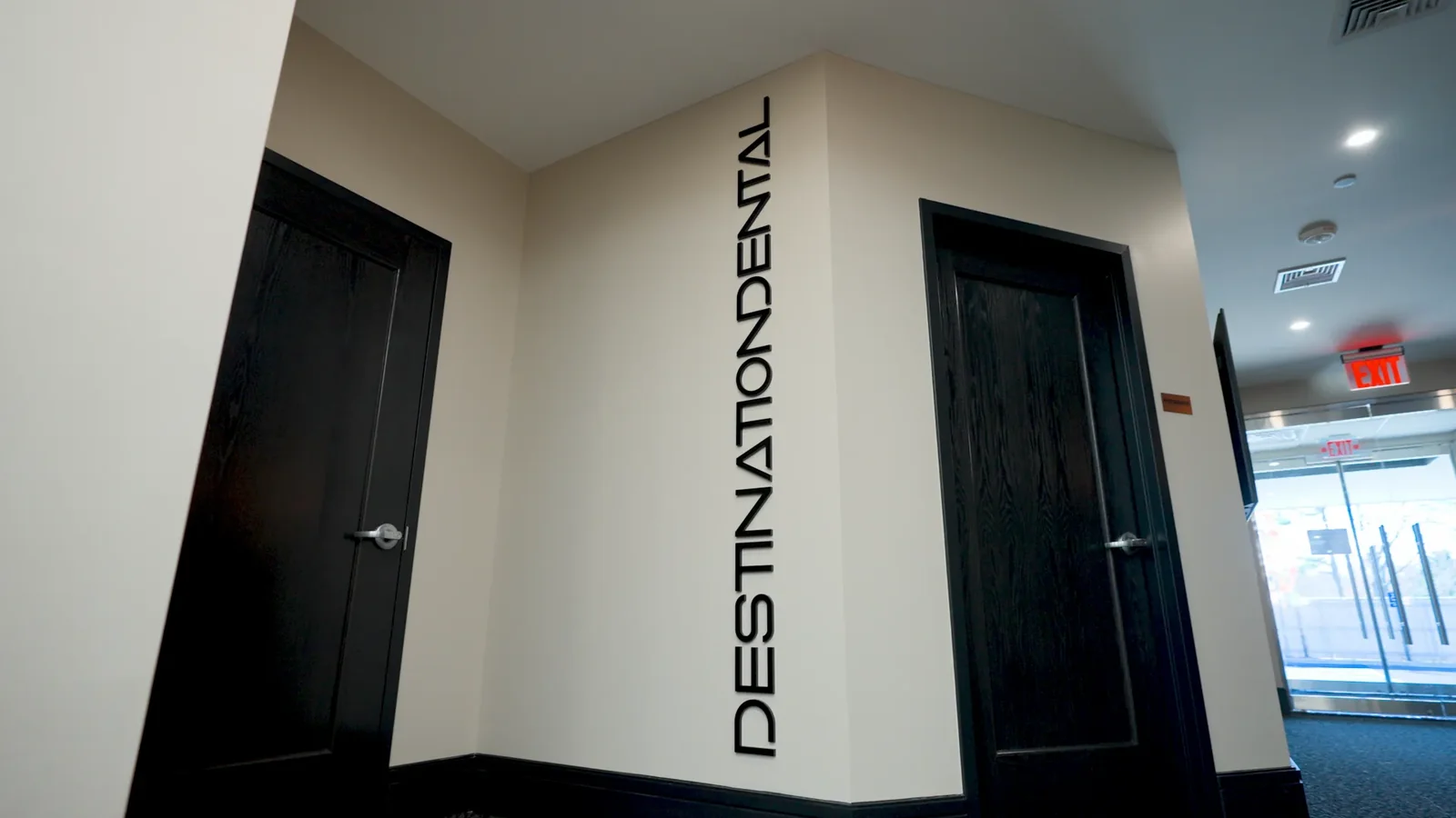 Destination Dental signage on the wall of the lobby at the practice's Hauppauge campus, between two dark doors