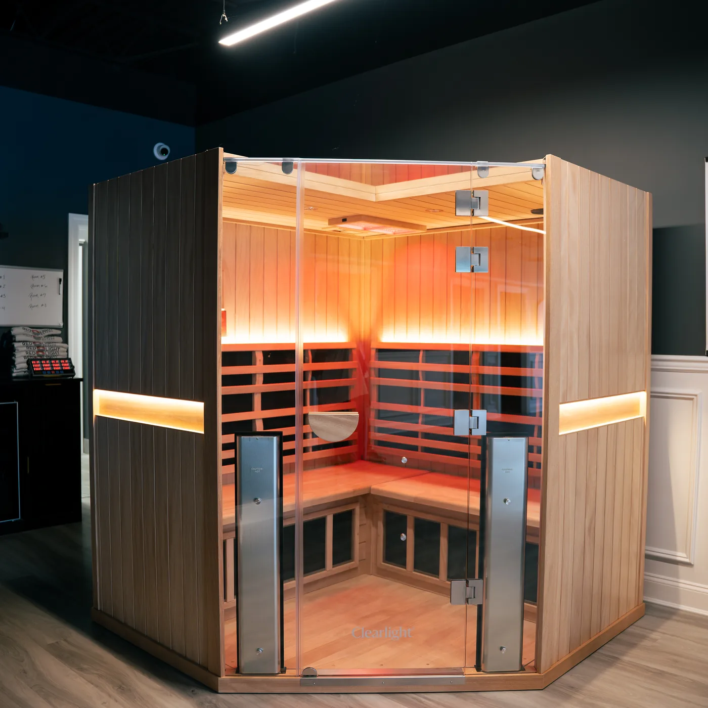 A cedar far infrared sauna cabin with a glass door, glowing warm from within, standing on the open floor at Red Light Method Commack