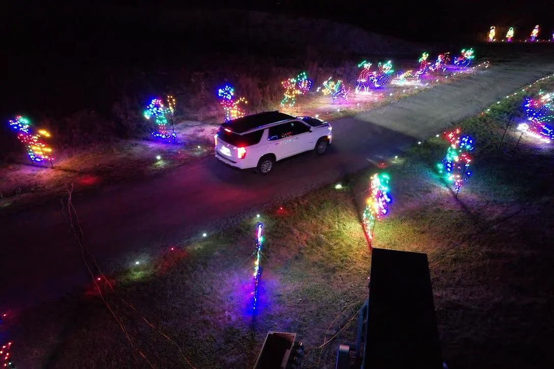 A white SUV drives a dark route lined with lit holiday figures at a Holiday Light Show
